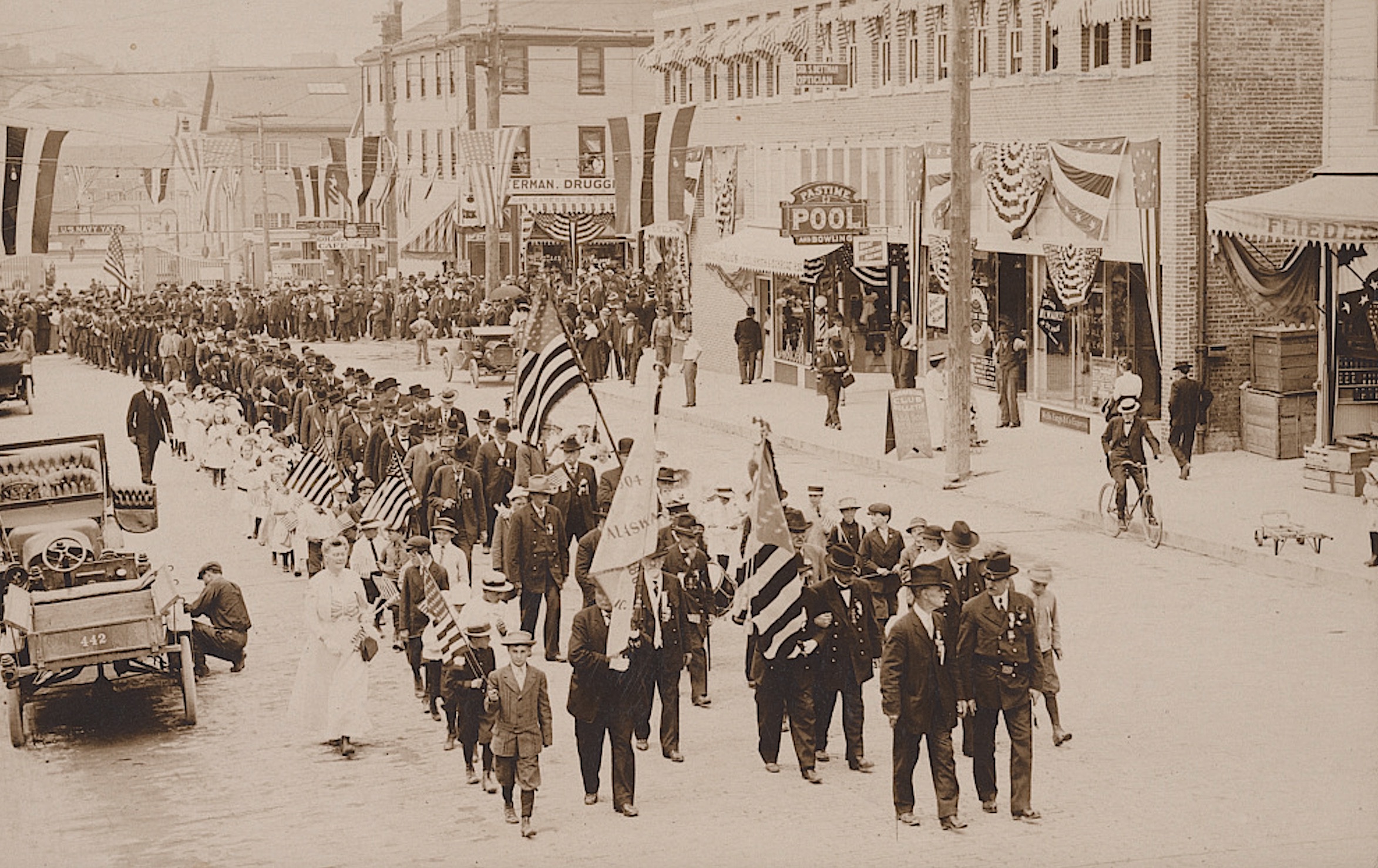 A parade of Civil War veterans and children carrying American and Alaska flags on an unidentified downtown street, sometime in the 1910s.